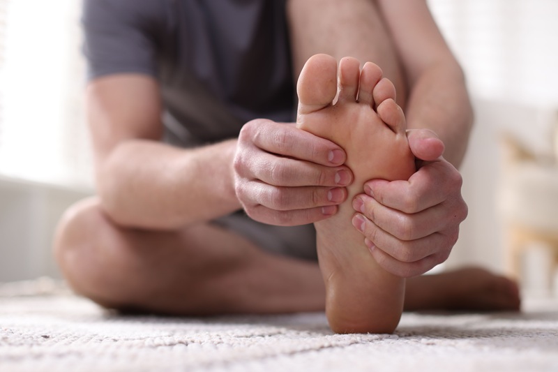 A man is clutching his foot, experiencing discomfort. It could be from plantar fasciitis