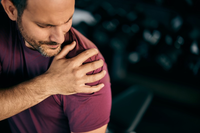 Close-up of a man holding his shoulder, injured during a workout at the gym.