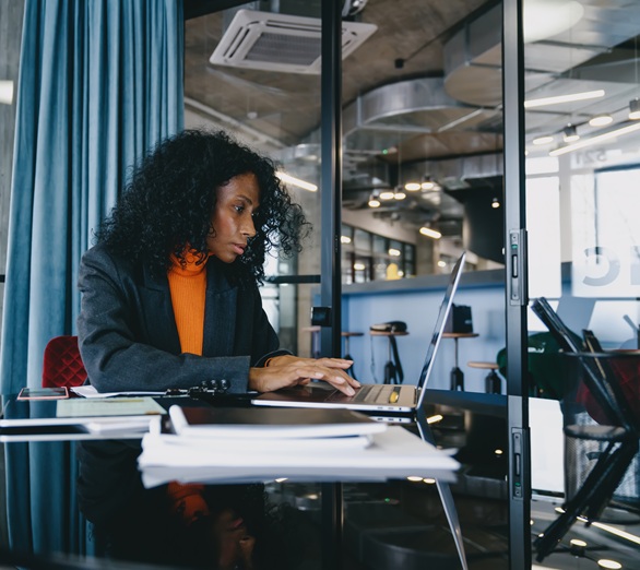 A corporate employee is typing on her laptop at her desk, staring down at the screen.