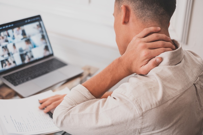 Close up rear image of a man working at his laptop. He is staring down at the screen and rubbing his neck in discomfort.