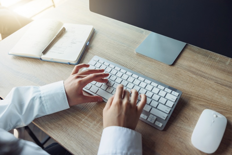 Close up of an office worker typing on a keyboard while sitting at a desk.