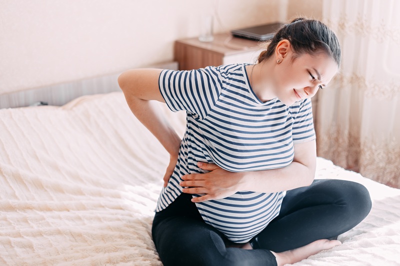 A pregnant woman is holding her back and side in discomfort.