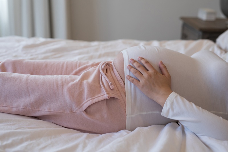 Close up image of a pregnant woman laying on her back in bed. Her hand is resting on her stomach.